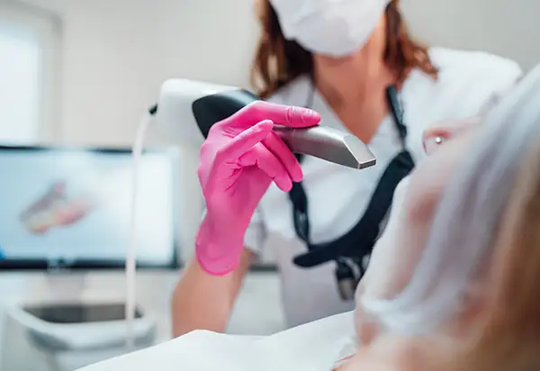 Close-up of a dental professional using a handheld digital impression scanner during a patient procedure, with 3D imaging results on a monitor in the background.